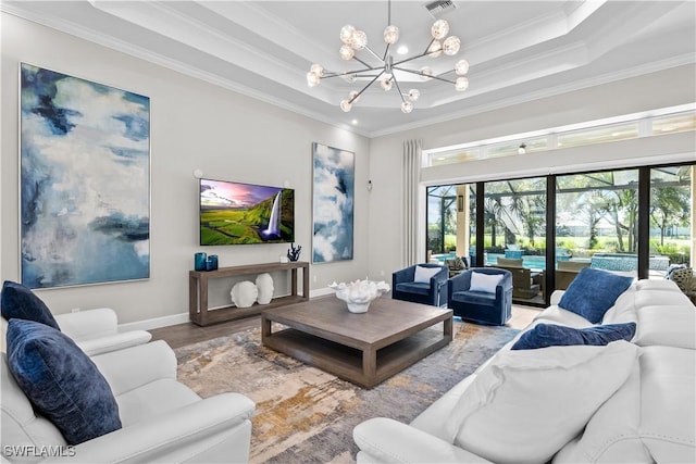 living room featuring ornamental molding, wood finished floors, a chandelier, baseboards, and a raised ceiling