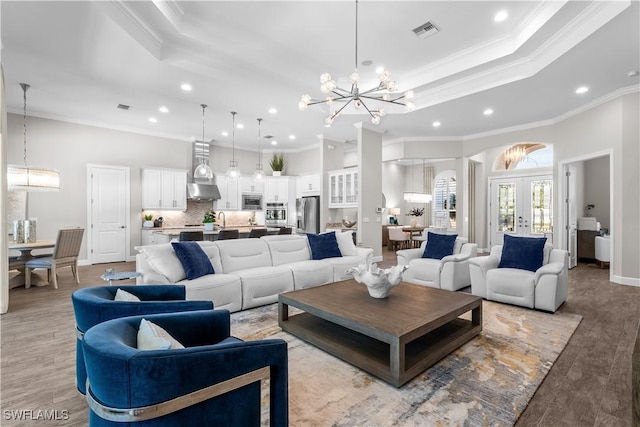 living room with a chandelier, ornamental molding, recessed lighting, light wood-style floors, and a raised ceiling