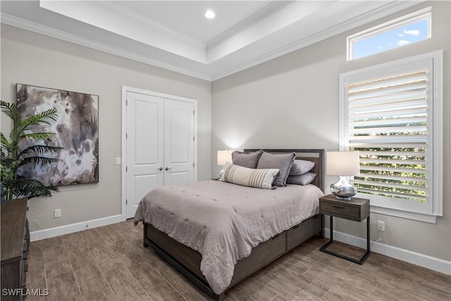 bedroom featuring crown molding, a raised ceiling, wood finished floors, baseboards, and recessed lighting