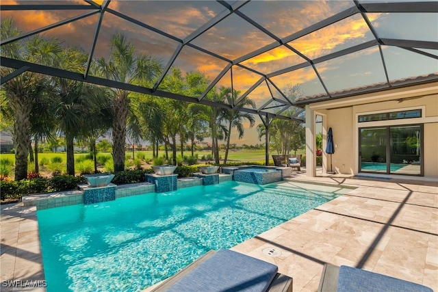 pool at dusk featuring a patio area, a pool with connected hot tub, and a lanai