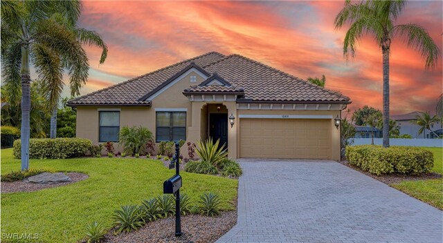 mediterranean / spanish-style house with driveway, a garage, a tile roof, stucco siding, and a yard