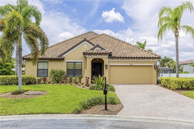 mediterranean / spanish-style home with stucco siding, an attached garage, a tiled roof, driveway, and a front lawn