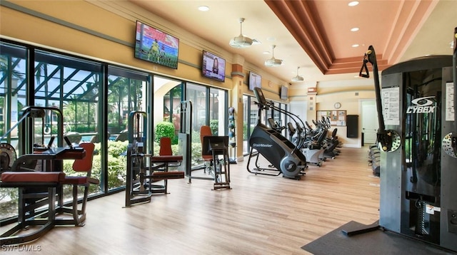 gym featuring a raised ceiling, recessed lighting, and wood finished floors
