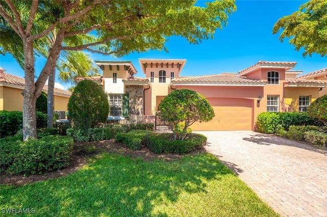 mediterranean / spanish house with a front lawn, a tile roof, stucco siding, decorative driveway, and an attached garage