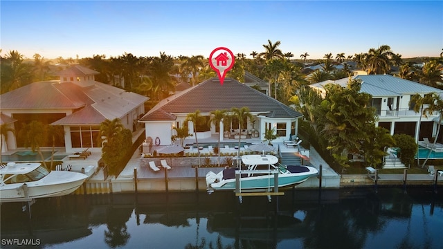 back of house at dusk with an outdoor pool, boat lift, a patio, and a water view