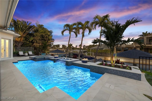 pool at dusk featuring fence, french doors, a pool with connected hot tub, and a patio