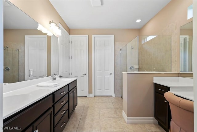 bathroom featuring tile patterned flooring, double vanity, a sink, baseboards, and tiled shower