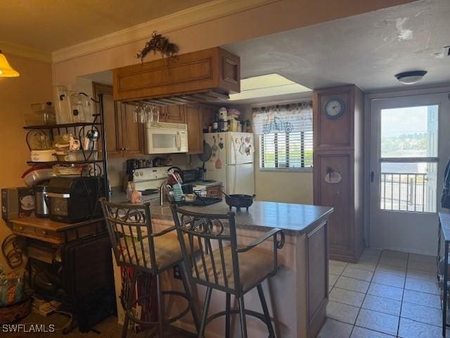 kitchen featuring crown molding, white appliances, light tile patterned floors, a peninsula, and brown cabinetry