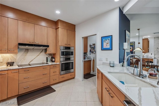 kitchen featuring light stone counters, a sink, stainless steel double oven, black electric stovetop, and under cabinet range hood