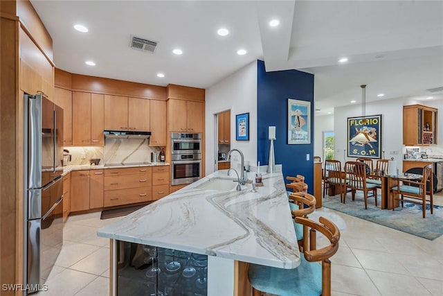 kitchen with visible vents, stainless steel double oven, a sink, light stone counters, and backsplash