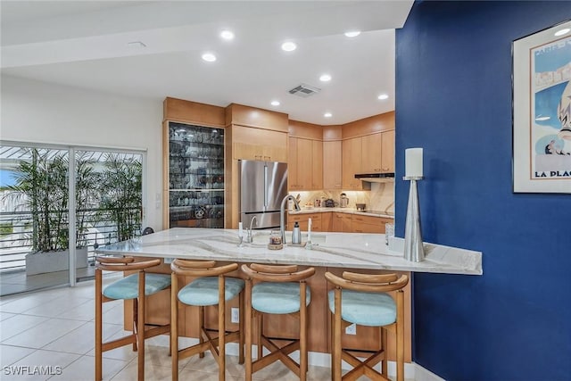 kitchen with light stone counters, freestanding refrigerator, a peninsula, light tile patterned floors, and visible vents