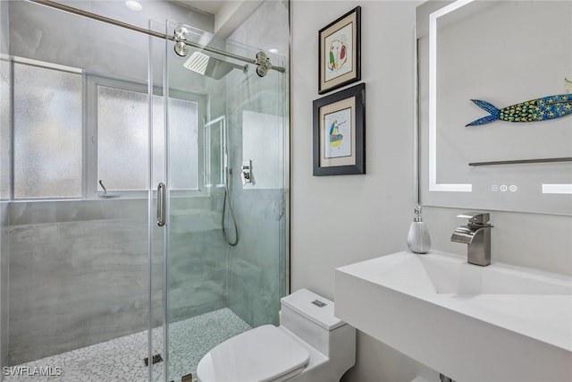 bathroom with a stall shower, toilet, a sink, and a healthy amount of sunlight