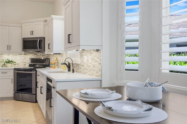 kitchen with light tile patterned floors, white cabinetry, appliances with stainless steel finishes, a sink, and backsplash