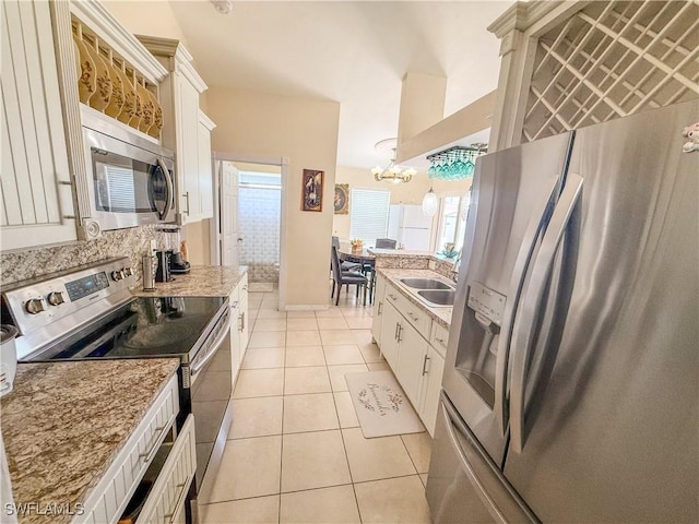 3911 9th St SW, Lehigh Acres, FL 33976 - kitchen with appliances with stainless steel finishes, a sink, white cabinets, an inviting chandelier, and light tile patterned flooring