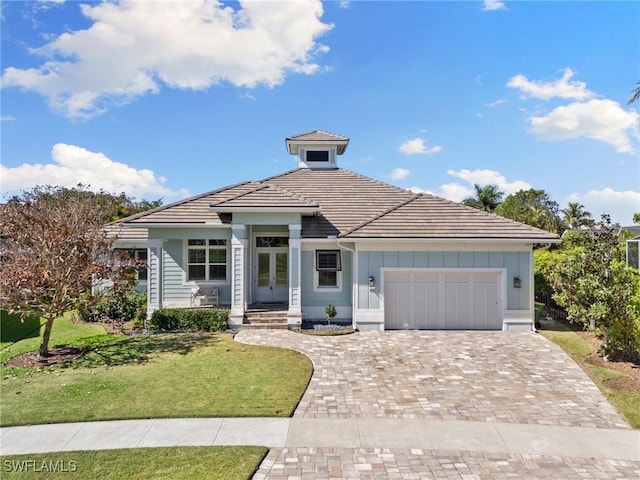 view of front facade featuring a tiled roof, an attached garage, board and batten siding, a front yard, and decorative driveway