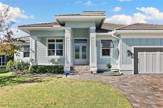 view of front facade with french doors, an attached garage, a front yard, and decorative driveway