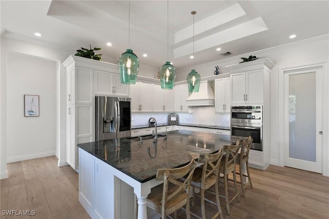 kitchen with a sink, white cabinets, custom range hood, backsplash, and appliances with stainless steel finishes