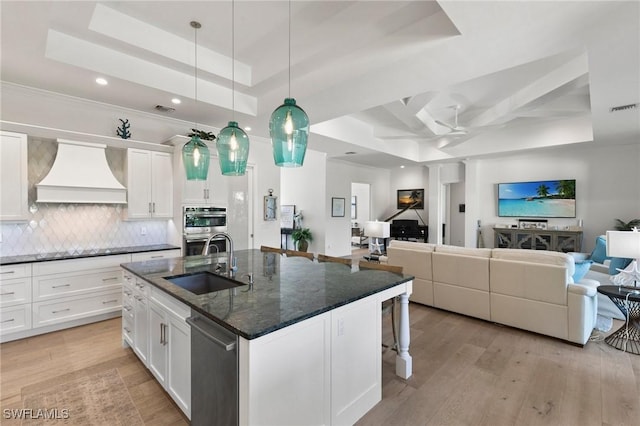 kitchen featuring a sink, open floor plan, custom range hood, a raised ceiling, and double oven