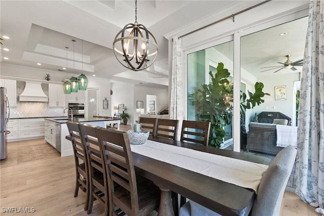 dining room with a raised ceiling, ceiling fan with notable chandelier, light wood-style floors, and recessed lighting