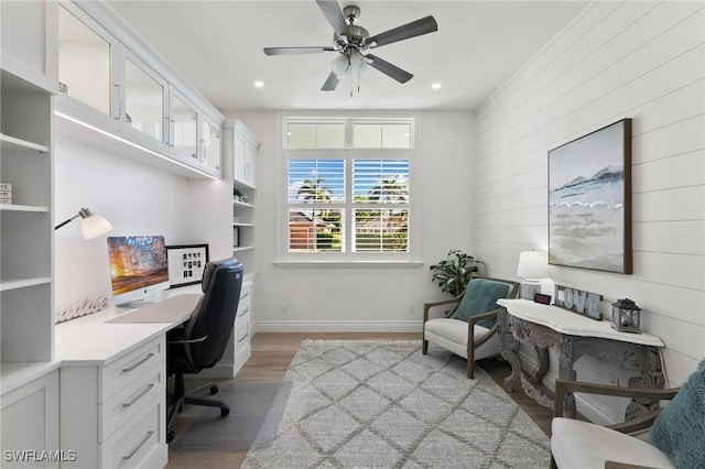 office with light wood finished floors, baseboards, built in desk, recessed lighting, and ceiling fan