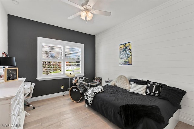 bedroom featuring light wood-type flooring, baseboards, an accent wall, a ceiling fan, and wooden walls