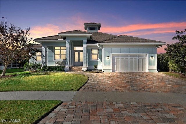 prairie-style house with a garage, a tiled roof, a front lawn, and decorative driveway