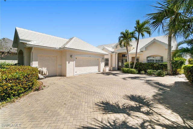 view of front of home featuring a tiled roof, decorative driveway, a garage, and stucco siding