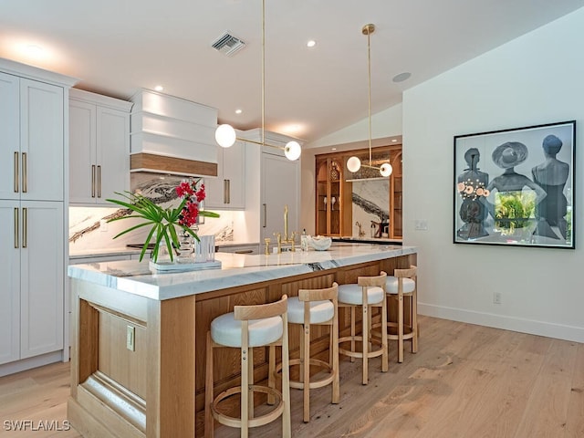 kitchen featuring white cabinetry, visible vents, a large island with sink, and light wood-style floors