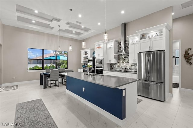 kitchen with wall chimney exhaust hood, stainless steel appliances, white cabinetry, an island with sink, and coffered ceiling