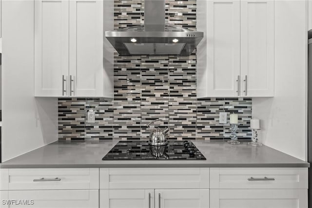 kitchen with wall chimney range hood, white cabinets, backsplash, and black electric cooktop