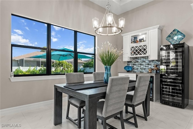 dining space featuring baseboards, a chandelier, marble finish floor, beverage cooler, and a bar