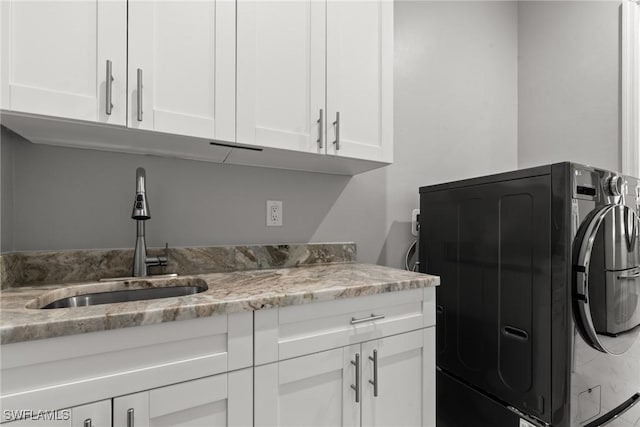 clothes washing area with washer / clothes dryer, cabinet space, and a sink