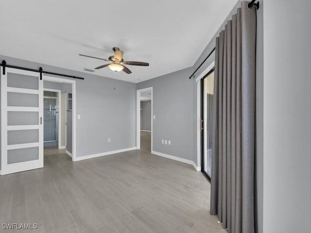 unfurnished bedroom featuring a barn door, a walk in closet, baseboards, and wood finished floors