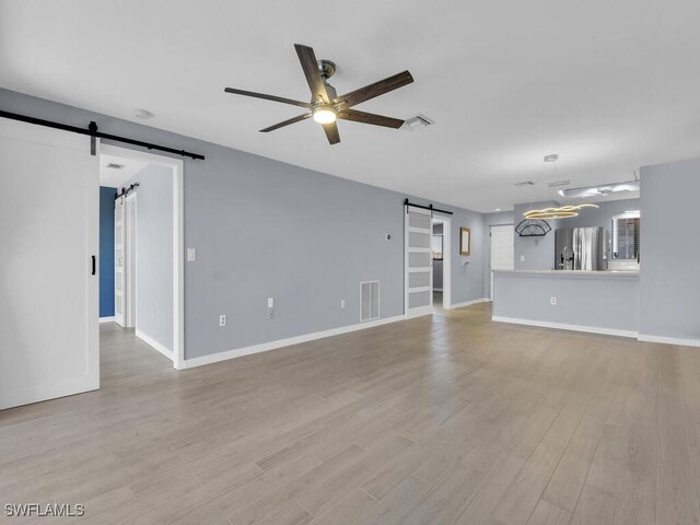 unfurnished living room with a barn door, a ceiling fan, light wood-style flooring, and baseboards