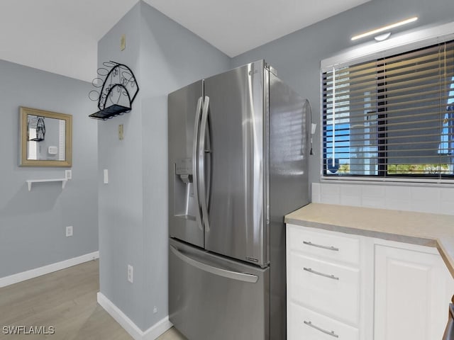 kitchen with stainless steel fridge with ice dispenser, white cabinetry, baseboards, light wood-style floors, and light countertops