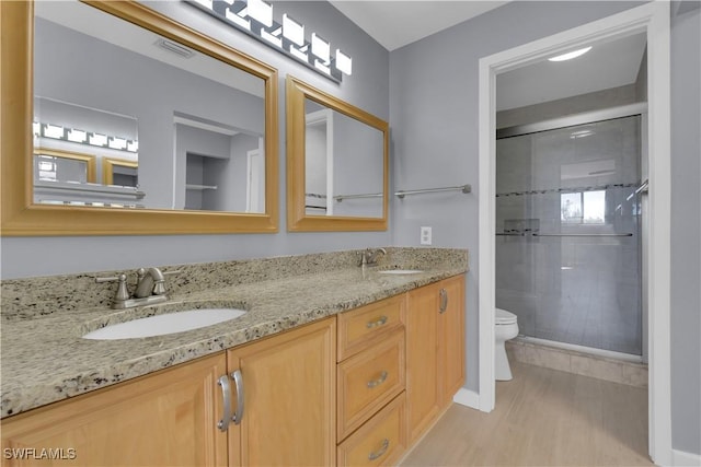 bathroom with toilet, a stall shower, double vanity, wood finished floors, and baseboards