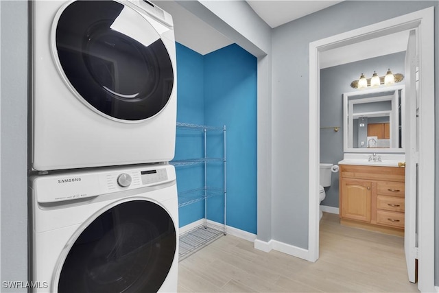 laundry area featuring estacked washer and dryer, light wood-style floors, and baseboards