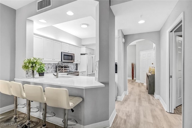 kitchen featuring visible vents, arched walkways, stainless steel appliances, light wood-style floors, and tasteful backsplash