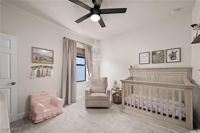 carpeted bedroom featuring a nursery area, a ceiling fan, and baseboards