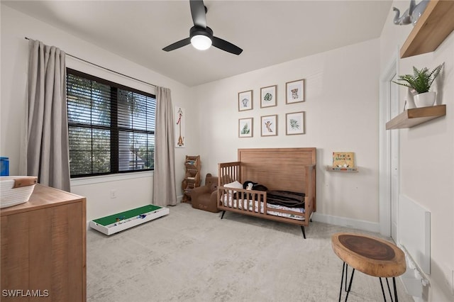 carpeted bedroom with baseboards, a crib, and ceiling fan