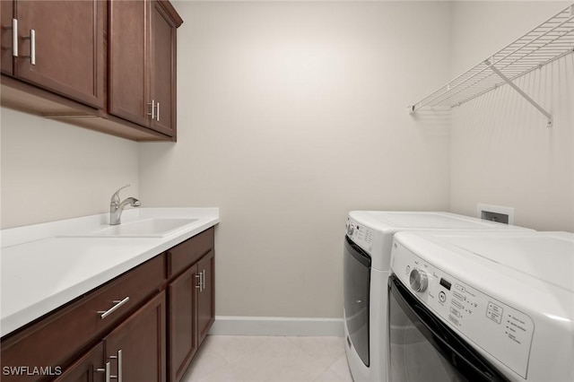 clothes washing area featuring washing machine and dryer, cabinet space, baseboards, and a sink