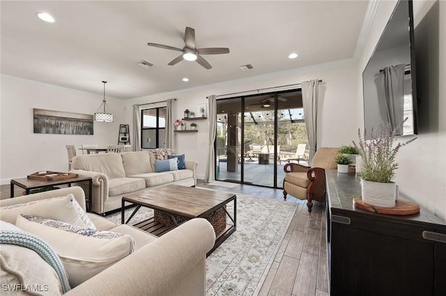 living room featuring ceiling fan, wood finished floors, visible vents, and ornamental molding