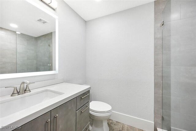 full bath with visible vents, toilet, a tile shower, vanity, and wood finished floors