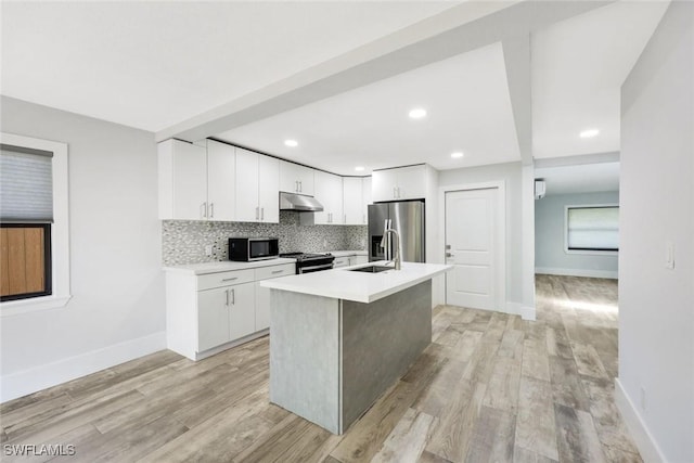 kitchen with a sink, light countertops, under cabinet range hood, stainless steel appliances, and decorative backsplash