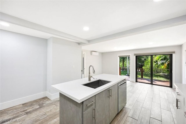 kitchen with light wood-style floors, dishwasher, light countertops, a sink, and a kitchen island with sink