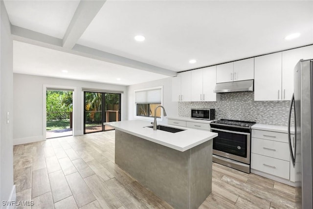 kitchen featuring a sink, under cabinet range hood, wood finish floors, stainless steel appliances, and decorative backsplash