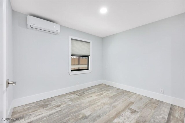 spare room featuring a wall mounted AC, wood finished floors, and baseboards