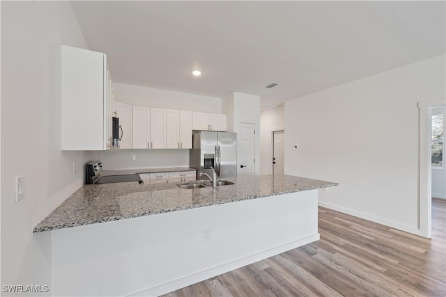 kitchen with white cabinets, a peninsula, light stone countertops, stainless steel appliances, and a sink