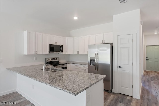kitchen with light stone countertops, a peninsula, dark wood-style floors, stainless steel appliances, and white cabinets
