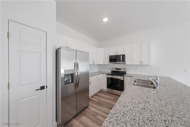 kitchen featuring white cabinets, light wood finished floors, stainless steel appliances, a sink, and light stone counters